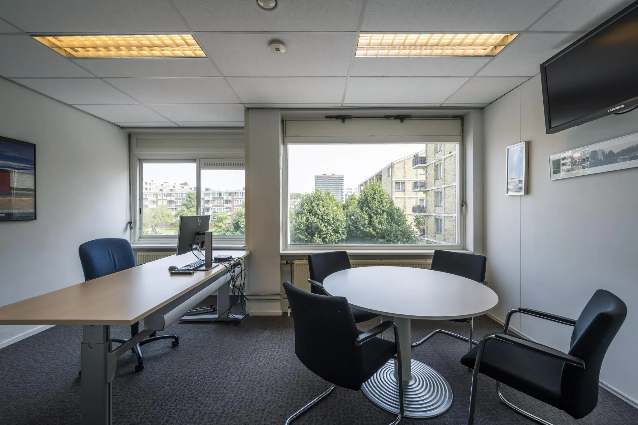 Modern ingericht kantoor aan de Jan Tooropstraat met een bureau, vergadertafel en uitzicht op omliggende flats.